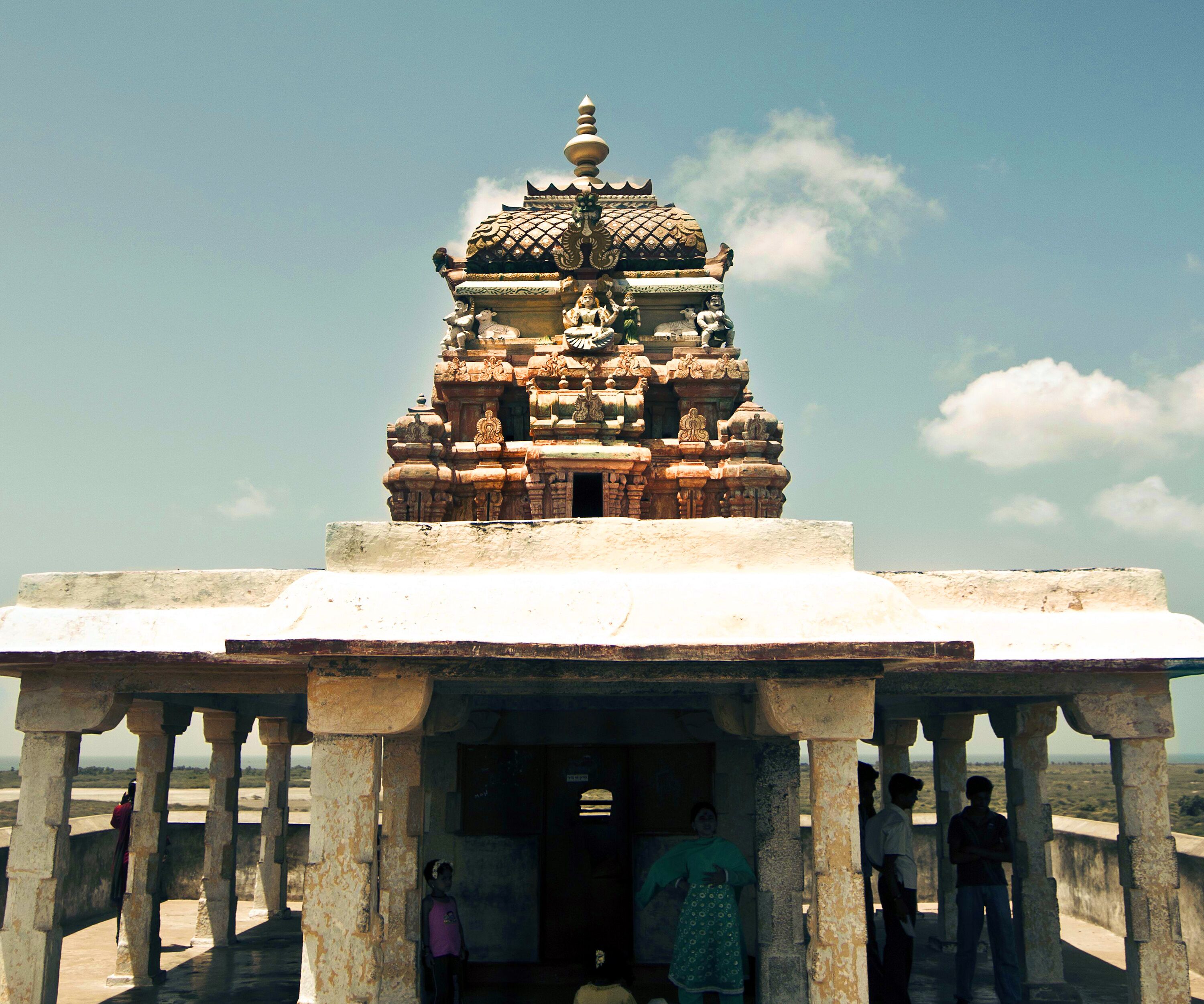 A temple with intricate carvings and a domed roof, viewed from a covered walkway.