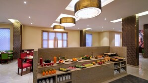 A buffet setup with various food items and beverages, a seating area with chairs, and a decorative wall with a floral pattern. - Daiwik Hotels Rameswaram (Rameshwaram)