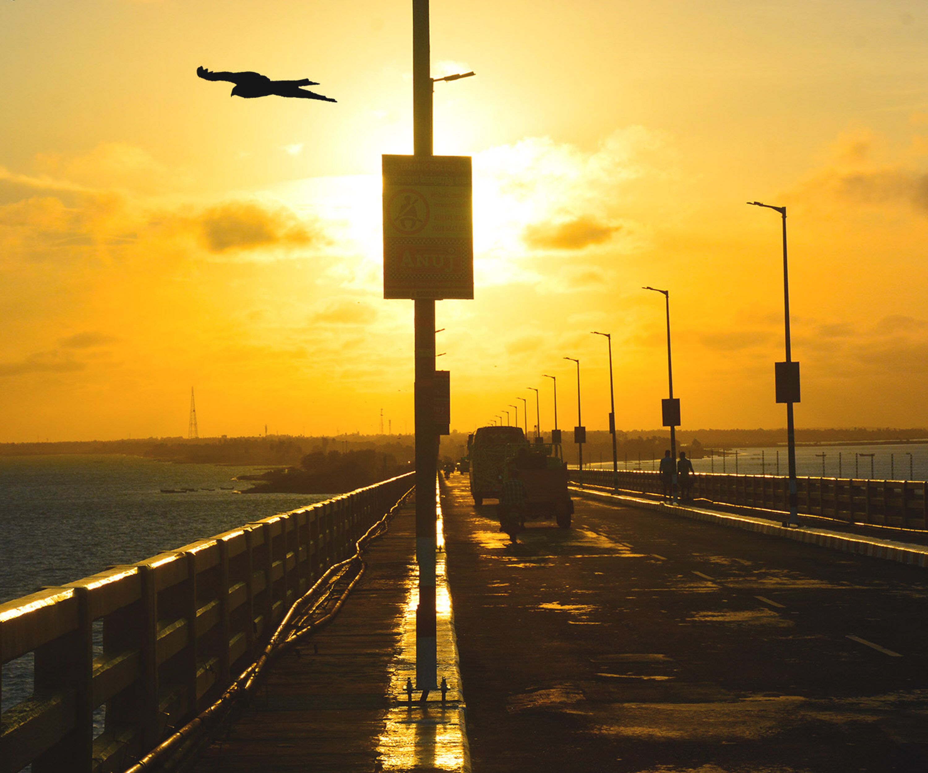 Un puente con farolas y un cartel, con vista a un cuerpo de agua al atardecer.