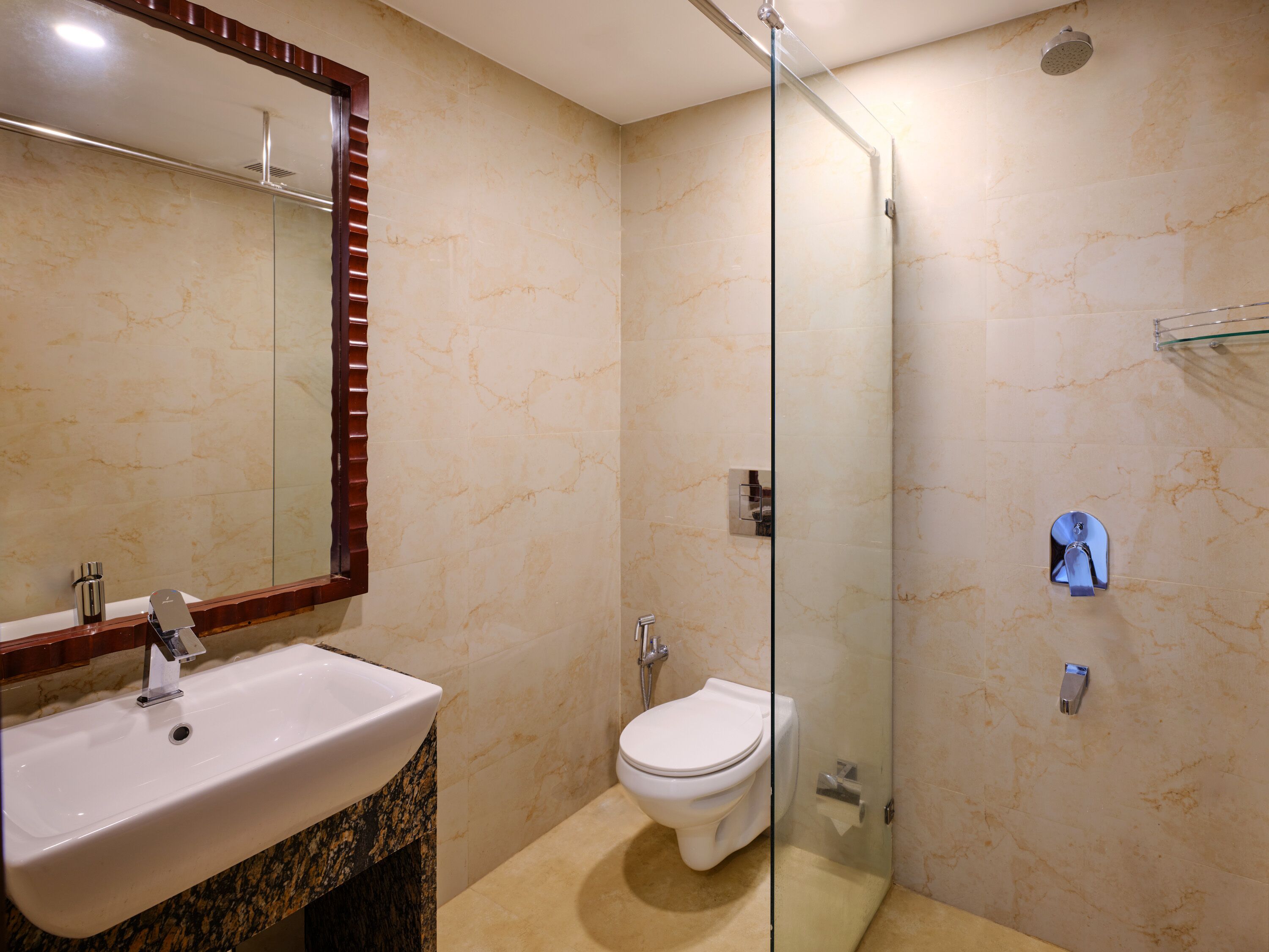 Un baño con pared de mármol, cabina de ducha de vidrio, lavamanos blanco y un inodoro.