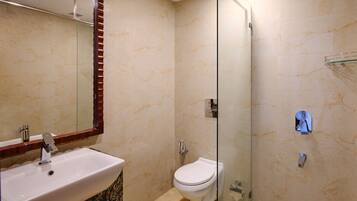 Un baño con pared de mármol, cabina de ducha de vidrio, lavamanos blanco y un inodoro.