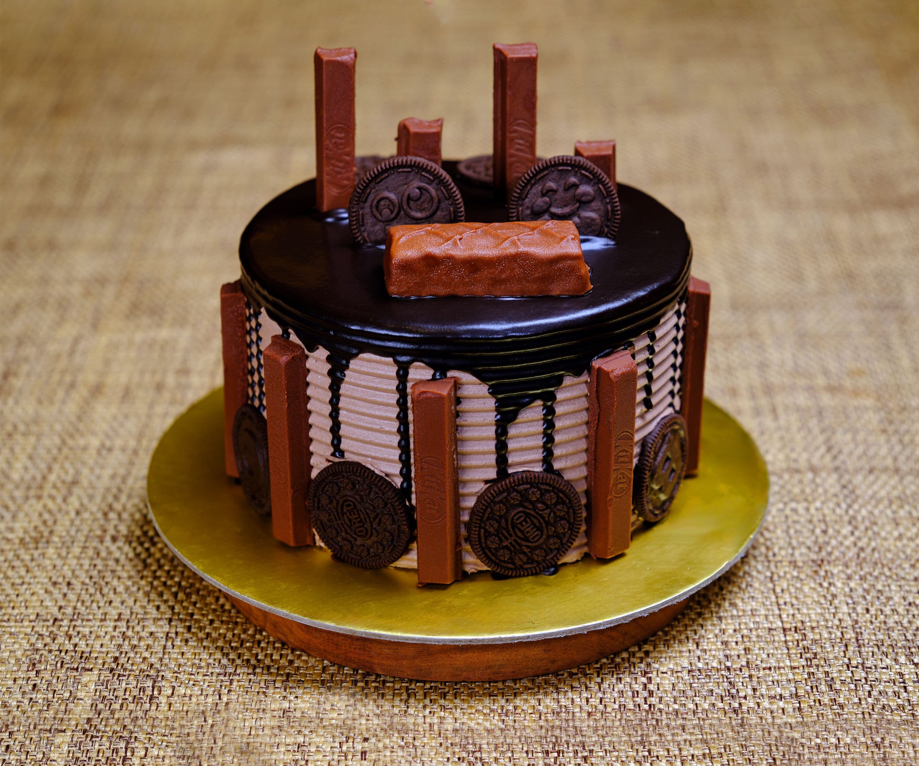 A small, round cake with chocolate decorations and Oreo cookies on a golden plate.