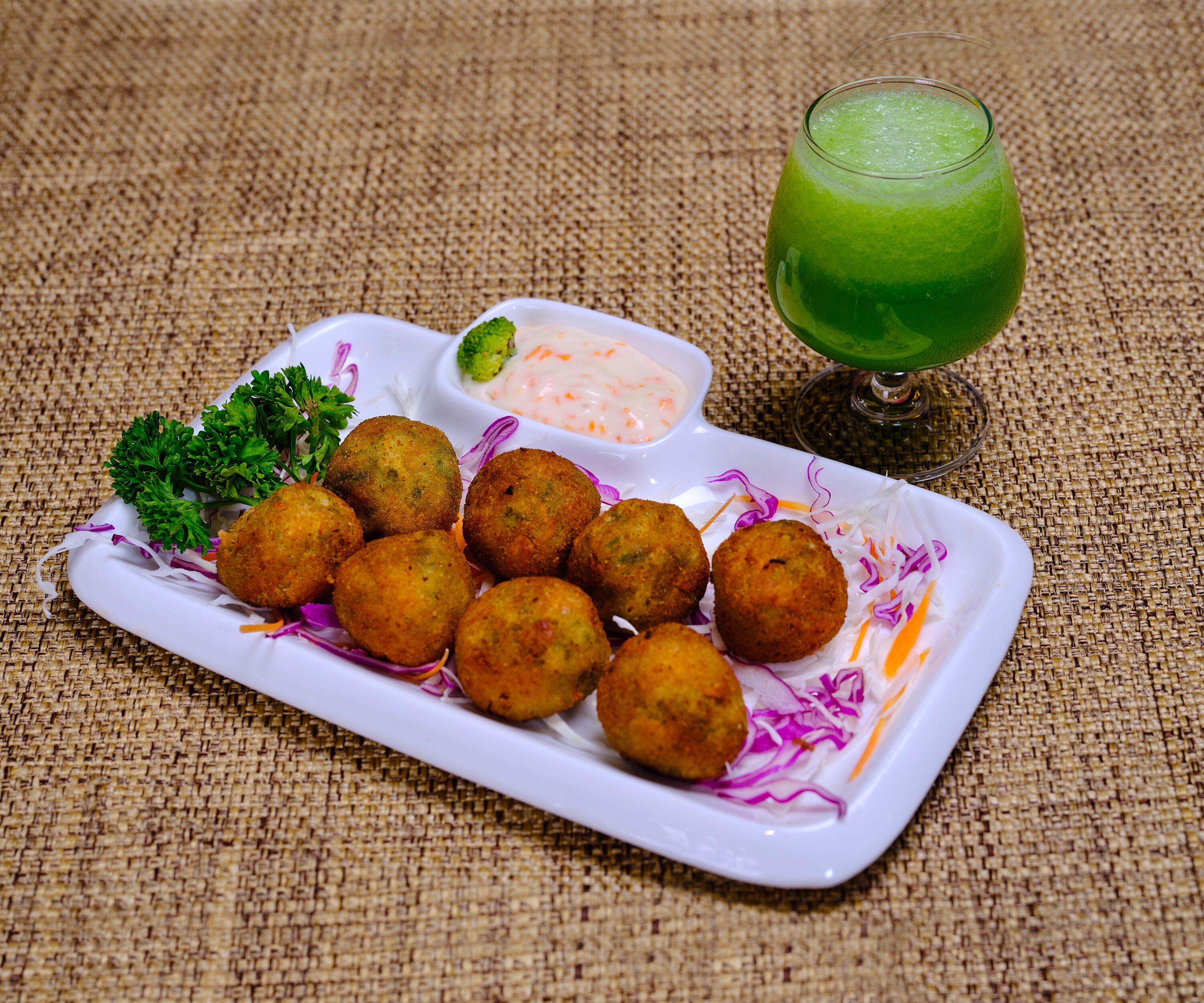 Un plato de bolitas fritas, ensalada de col y una bebida verde sobre un mantel texturizado.