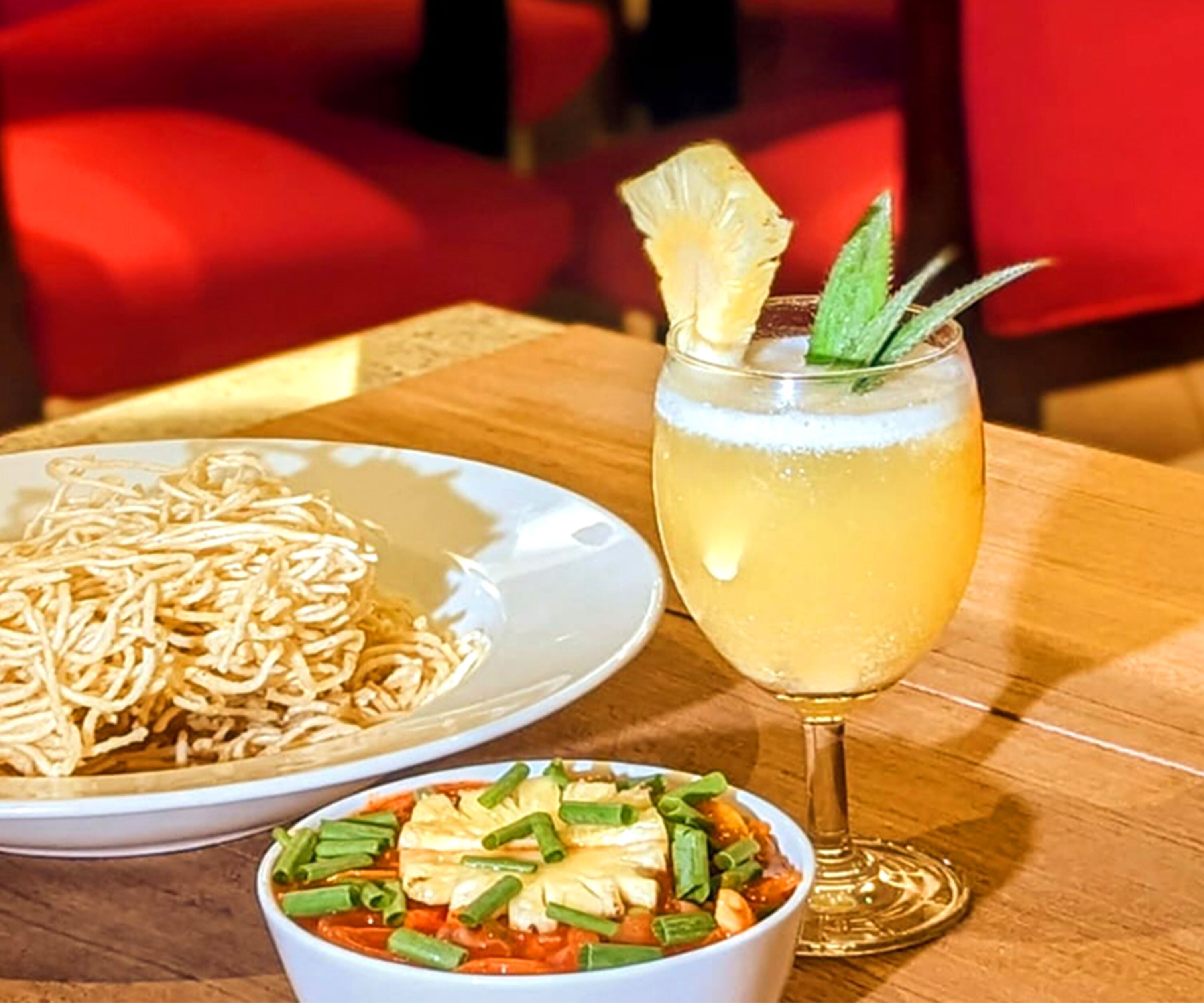 Une table avec une assiette de nouilles, un bol de soupe aux légumes et un verre d’une boisson jaune, agrémentée d’une garniture.