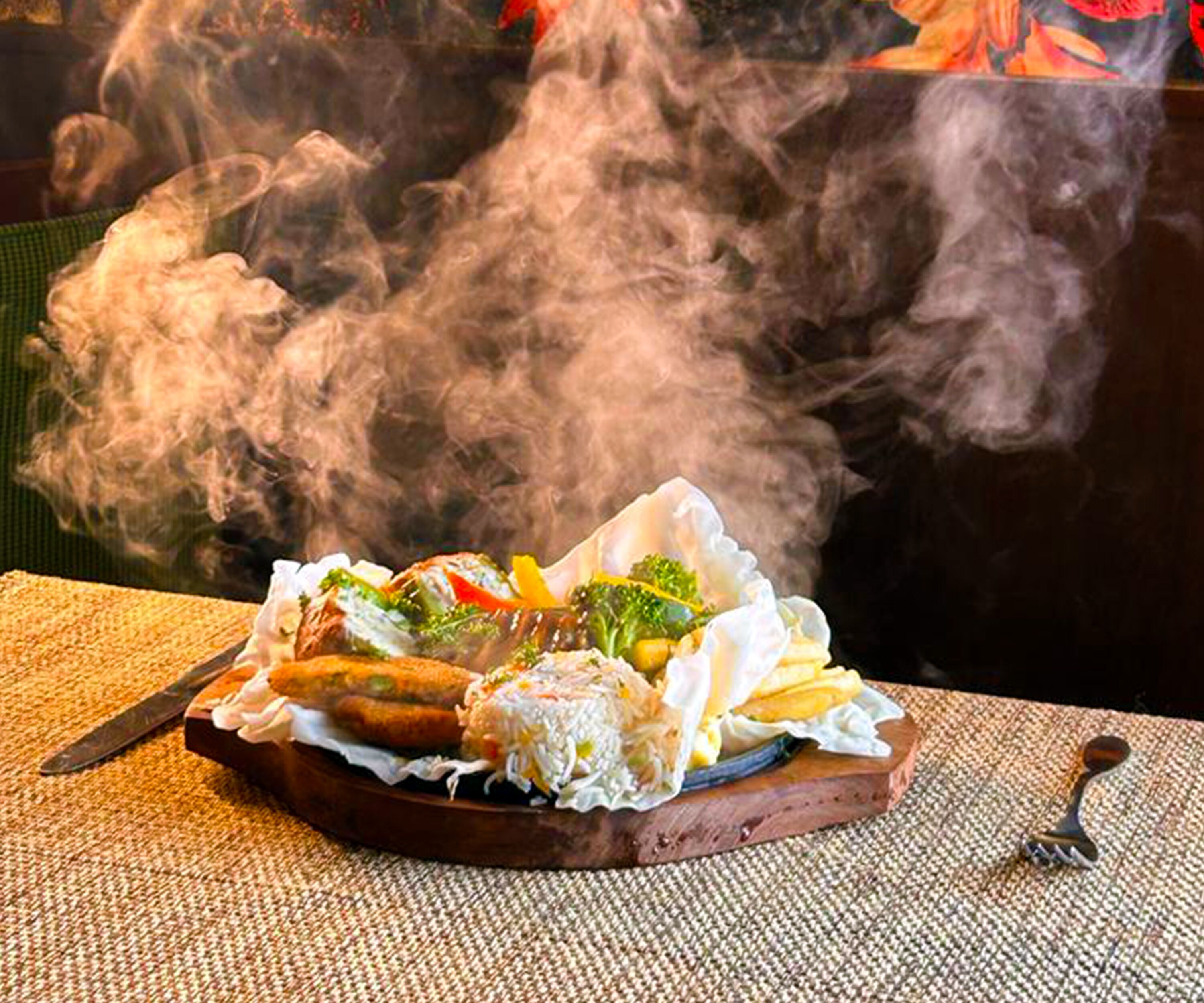 A meal with a variety of vegetables and a piece of meat, served on a wooden board with a knife and fork on the side.