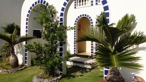 A building with three arched doorways, each with blue-tiled accents. There are potted plants and a palm tree in the foreground. - Squares Cafe and Apartments (Puerto Galera)