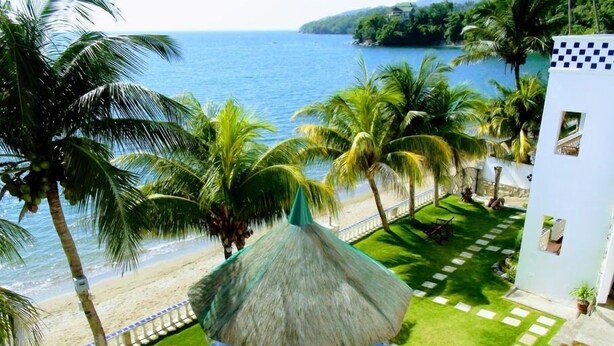 A beachside patio with a thatched umbrella, palm trees, and a view of the sea. - Squares Cafe and Apartments (Puerto Galera)