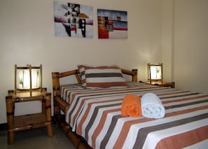 A neatly made bed with striped bedding, two bedside tables with lamps, and two wall-mounted paintings.