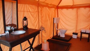 A compact tent bathroom with a sink, mirror, lantern, toilet, and a small table with towels. - Camp Tapovan Nasik (Trimbak)