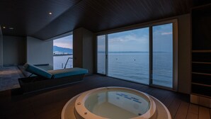 A modern room with a large window, a hot tub, and a seating area with a view of the sea.