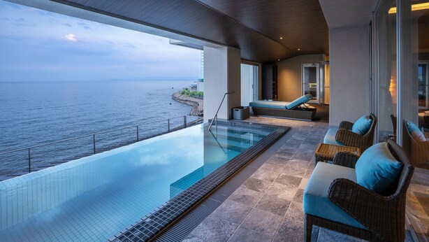 Una piscina infinita moderna con vistas despejadas al mar, una zona de estar acogedora con mobiliario de mimbre y un diseño interior contemporáneo.