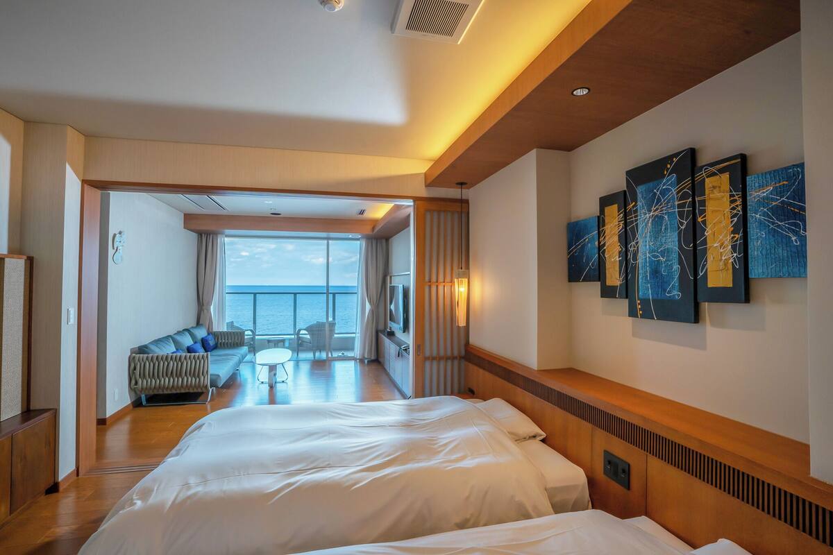 Quarto de hotel moderno com uma cama grande, um sofá e varanda com vista.