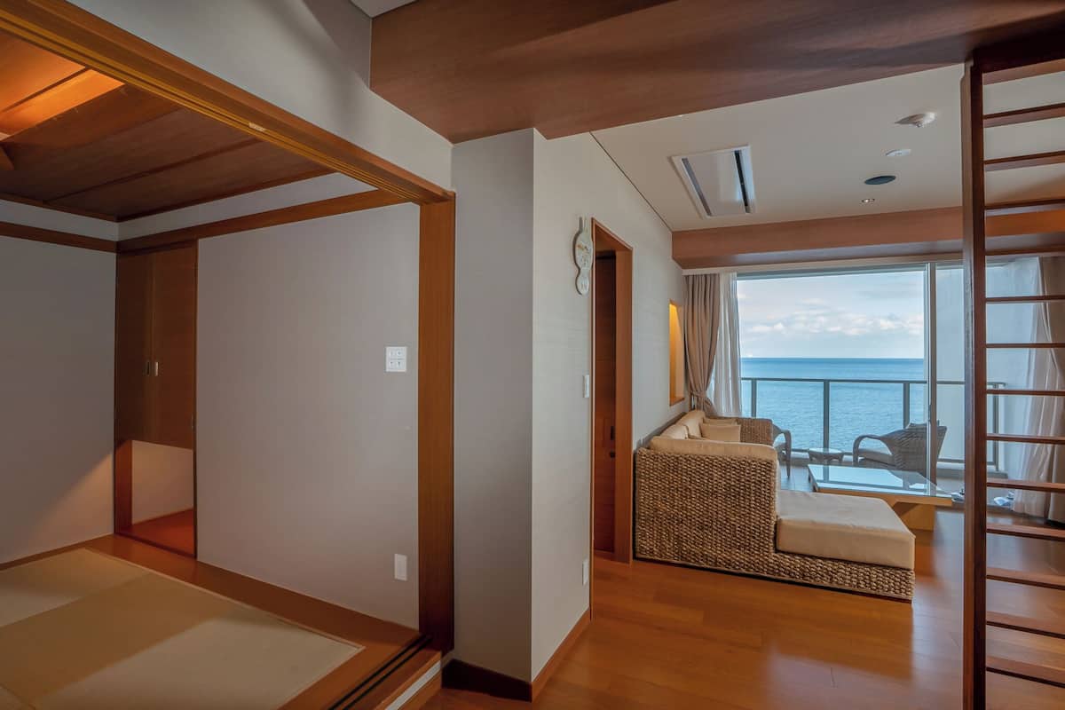 Quarto com teto de madeira, uma grande janela com vista para o mar, um sofá e uma pequena mesa.