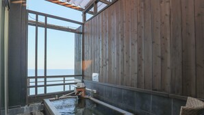 Un spa de madera con un jacuzzi, vistas al mar y sillones de mimbre.