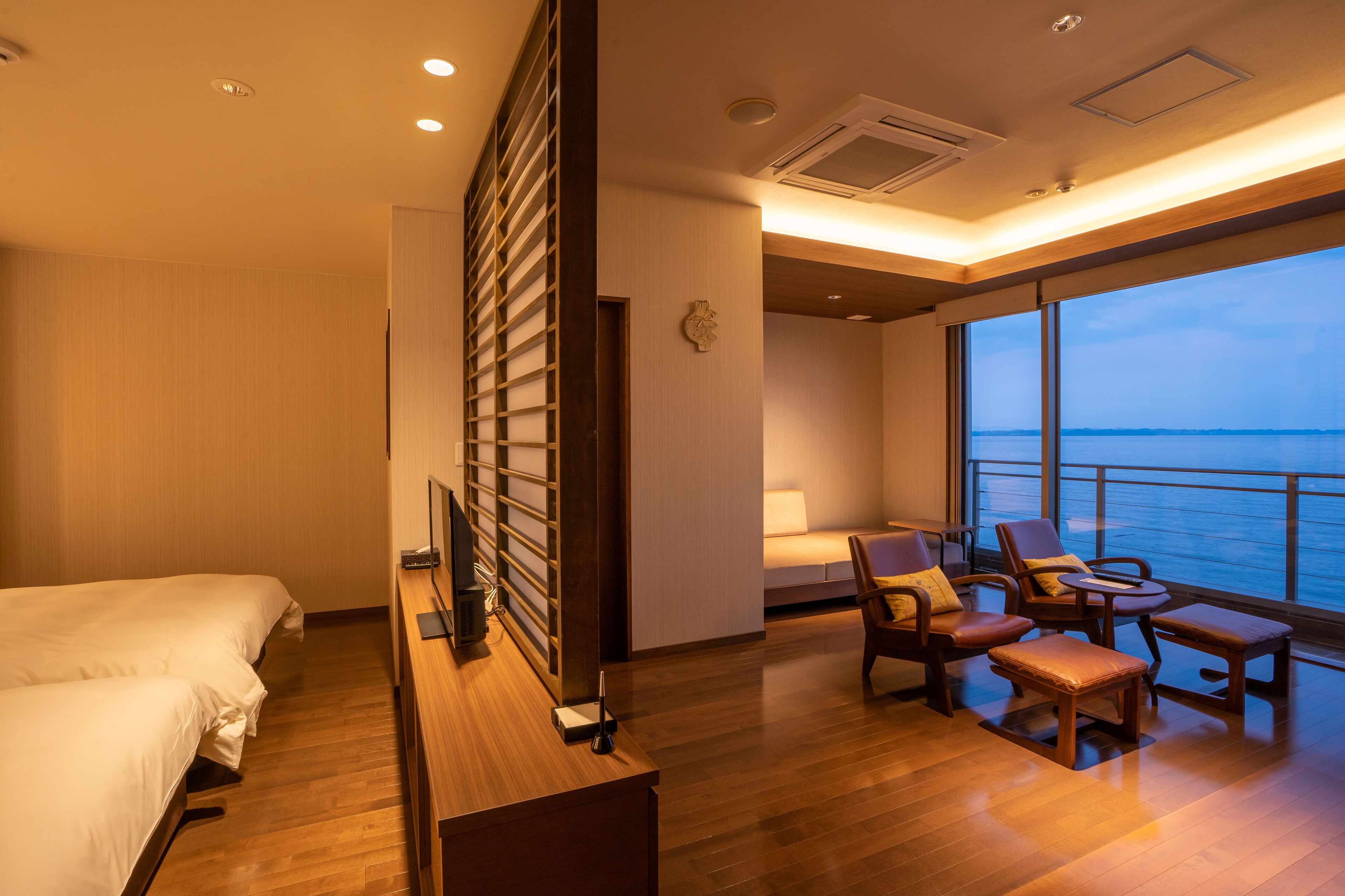 Habitación de hotel con cama, escritorio, silla, mesa y un amplio ventanal con vistas al mar.