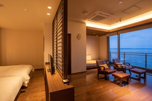 Habitación de hotel con cama, escritorio, silla, mesa y un amplio ventanal con vistas al mar.