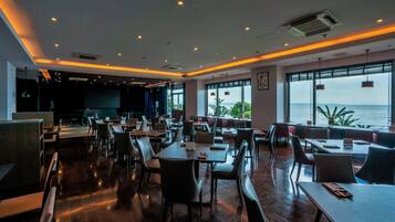 A spacious restaurant with high tables and chairs, large windows with a view of the sea, and a modern interior design.