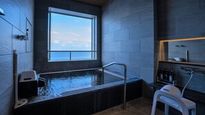 Un baño moderno con una bañera grande, una ventana y un taburete blanco pequeño.