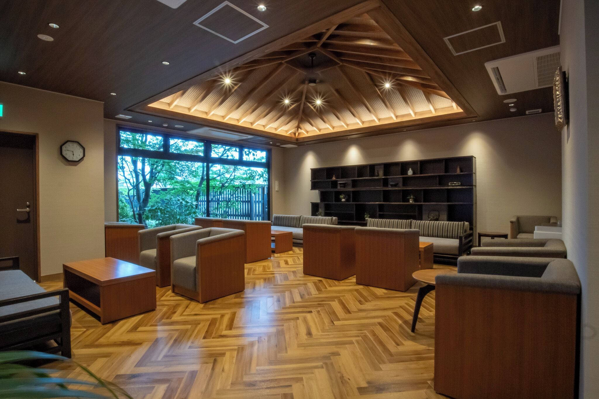 A modern lounge area with wooden flooring, sofas, and a bookshelf.