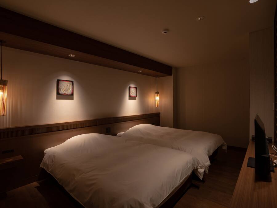 A hotel room with two beds, a wooden headboard, wall-mounted artwork, and a television on a wooden desk.