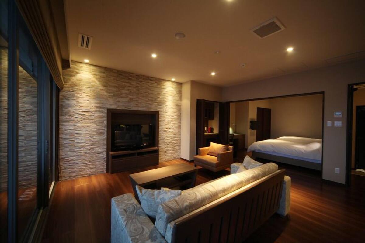 Ein modernes Hotelzimmer mit einer Wand aus Naturstein, einem Flachbildfernseher, einer Couch, einem Bett und einem kleinen Tisch.