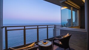 Un balcón con vista al océano, muebles de mimbre y una pequeña mesa con un objeto decorativo.