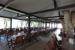 A covered outdoor dining area with rows of tables and chairs, large trees, and a tiled floor. - Club Yali Hotels & Resort - All Inclusive (Menderes)