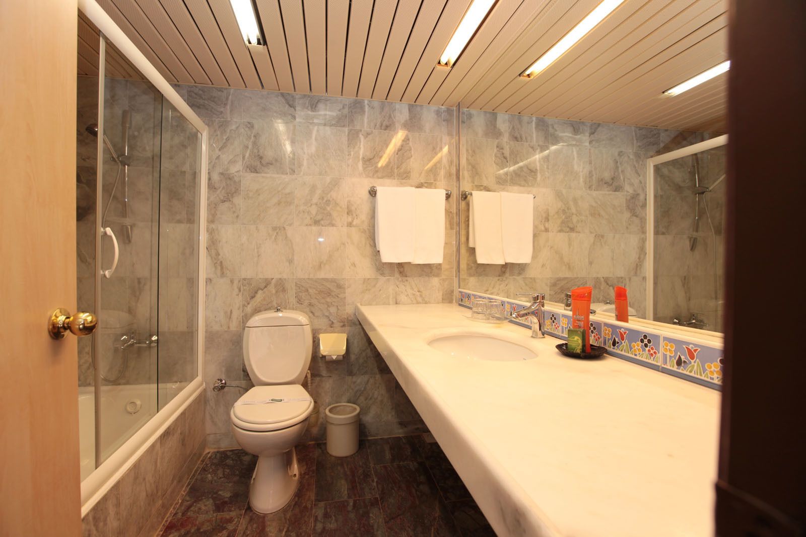 A bathroom with a marble floor, a toilet, a sink with a mirror, and a shower area.