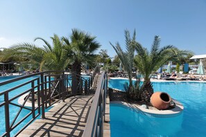 Un espace piscine comprenant plusieurs piscines, des palmiers et une terrasse en bois.