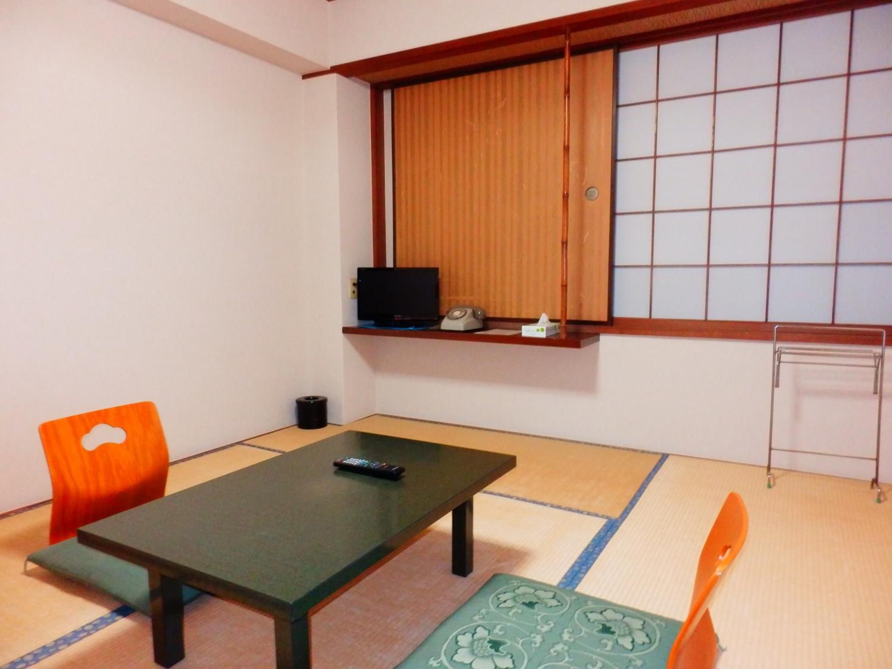 Una habitación con suelo de tatami, una mesa baja, un sofá, un televisor en un estante y un radiador.