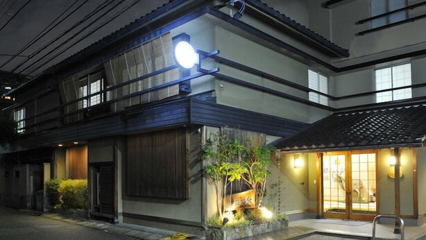 A traditional Japanese building with a wooden exterior, a small garden with plants and a stone lantern, and a sliding door entrance. - Nakayasu Ryokan (Kanazawa)