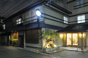 A traditional Japanese building with a wooden exterior, a small garden with plants and a stone lantern, and a sliding door entrance. - Nakayasu Ryokan (Kanazawa)