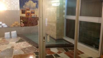 A bathroom with a tiled floor, a glass door, and a wall with a poster and some toiletries.