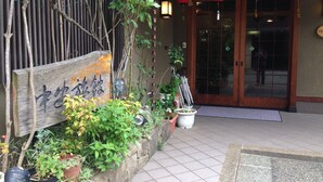 A traditional Japanese building entrance with a wooden sign, potted plants, and a tiled pathway leading to the door. - Nakayasu Ryokan (Kanazawa)