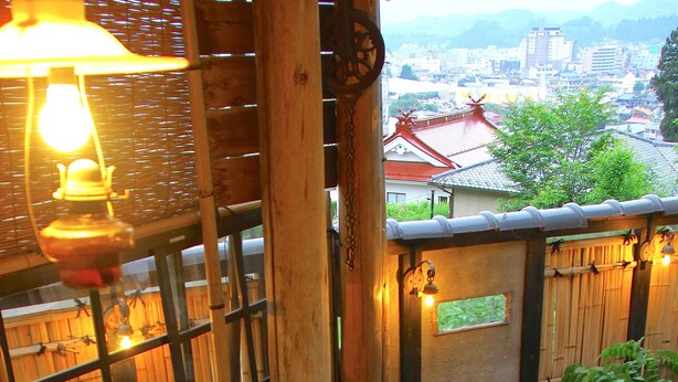 A hot spring bath area with a wooden fence, a lantern, and a view of buildings in the background. - Oyado Chogoro (Takayama)