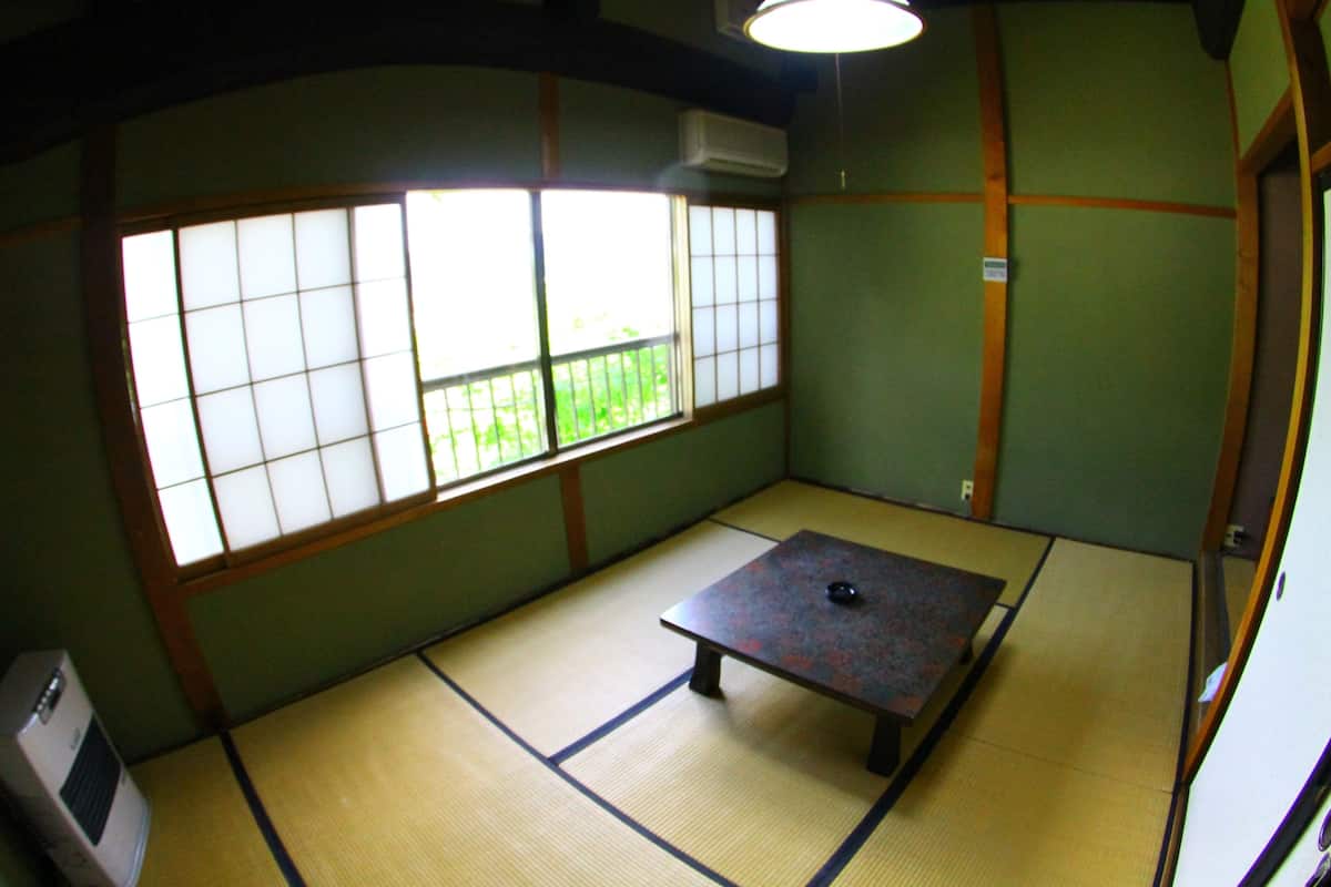 A tatami mat room with a tatami mat table, a heater, and a window with a view of greenery.