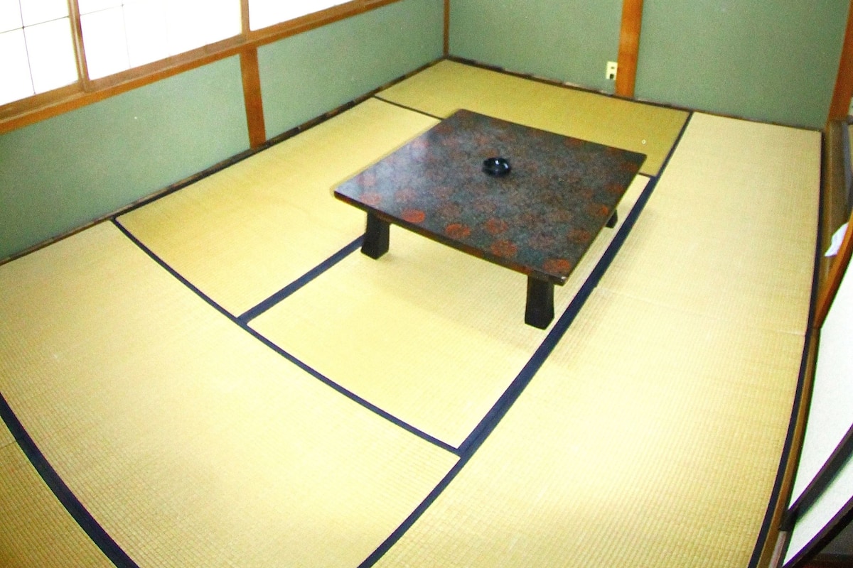 A tatami mat room with a low table, wooden beams, and a hanging light fixture.