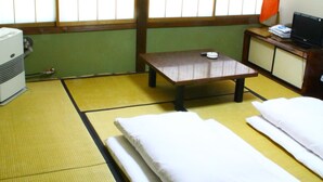 A traditional Japanese room with tatami flooring, a futon bed, a small table with a lamp, and a television on a cabinet. - Oyado Chogoro (Takayama)
