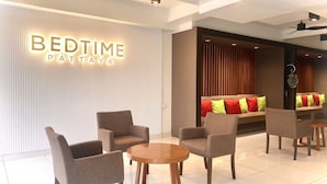 Um lobby de hotel moderno com um letreiro 'BEDTIME PATTAYA', área de estar com sofás e cadeiras, e um balcão de recepção.