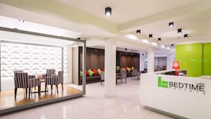 Uma área de recepção de hotel com design moderno, apresentando um balcão de atendimento, sala de estar com cadeiras listradas e uma parede estampada.