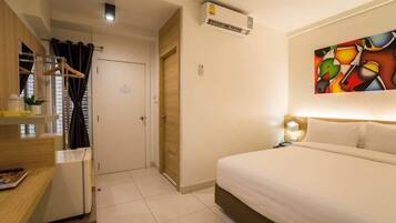 A hotel room with a bed, a desk, a wardrobe, and an air conditioning unit.