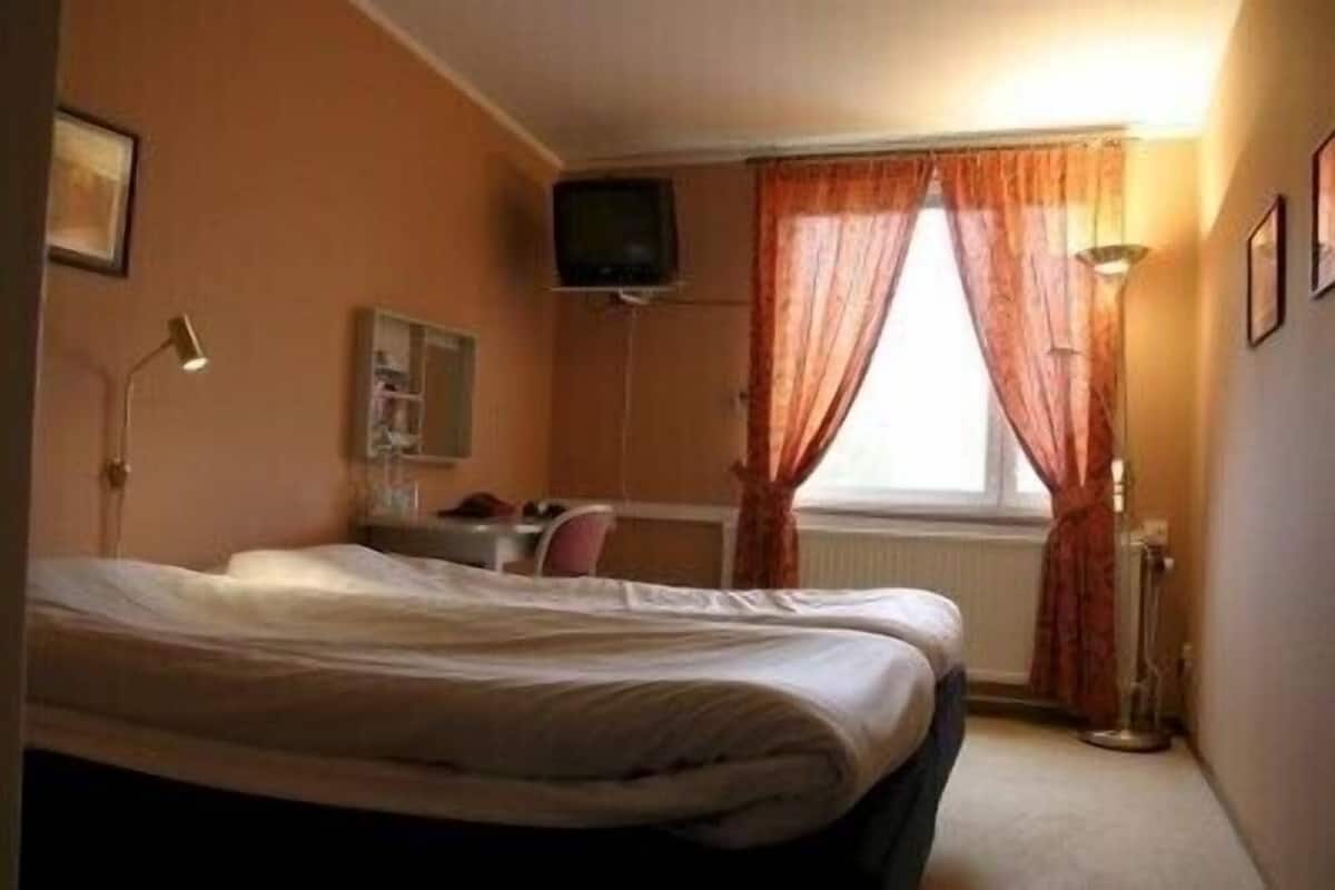 Habitación de hotel con cama, escritorio, silla, televisor y ventana con cortinas.