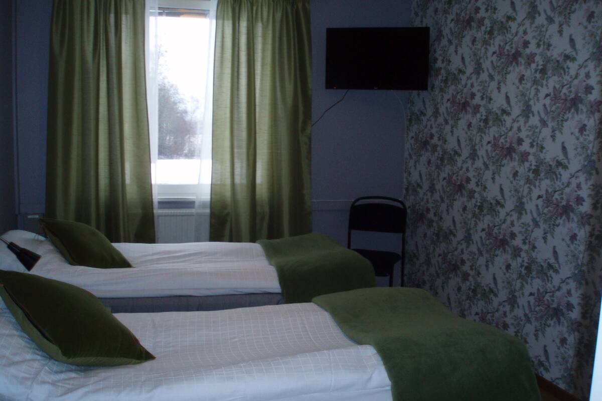 Una habitación con dos camas, una silla, un televisor y un ventanal con cortinas.