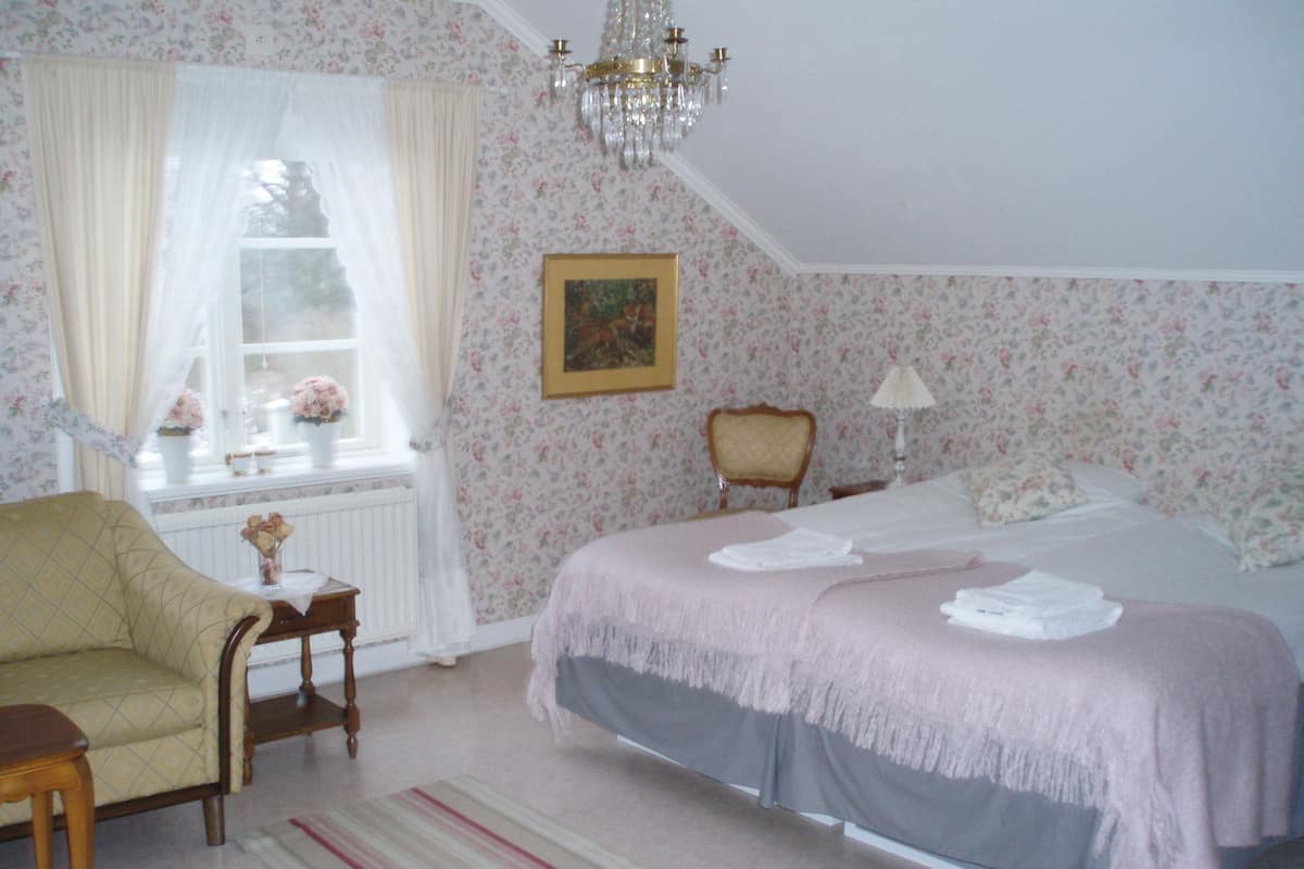 Un dormitorio con una cama, una silla, una mesa, una araña y una ventana con cortinas.