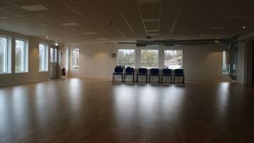 A spacious room with a wooden floor, large windows, and blue chairs arranged in a row.
