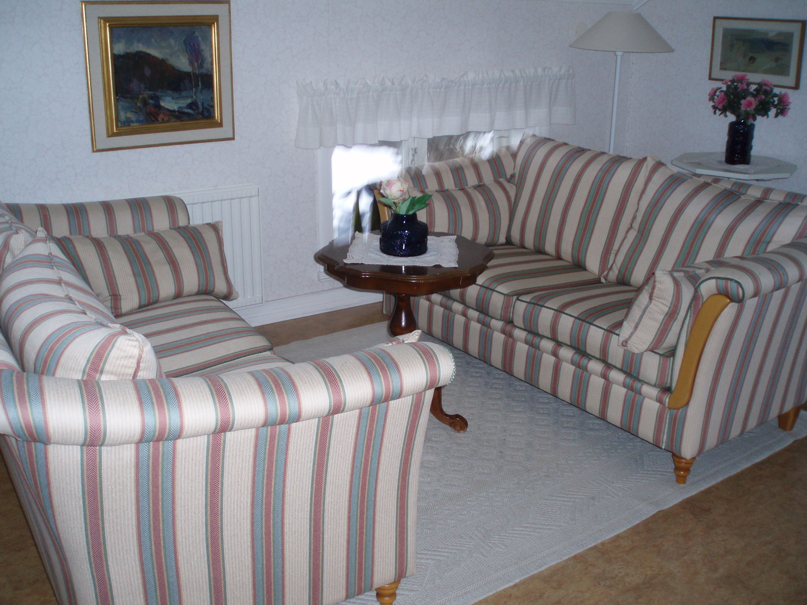 Ein Wohnzimmer mit gestreiften Sofas und Sesseln, einem kleinen Tisch mit einer Vase sowie einer Lampe.