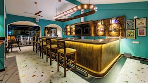 A bar area with wooden bar stools, a curved bar counter, and a television mounted on the wall. - Hotel Lua Nova (Baga)