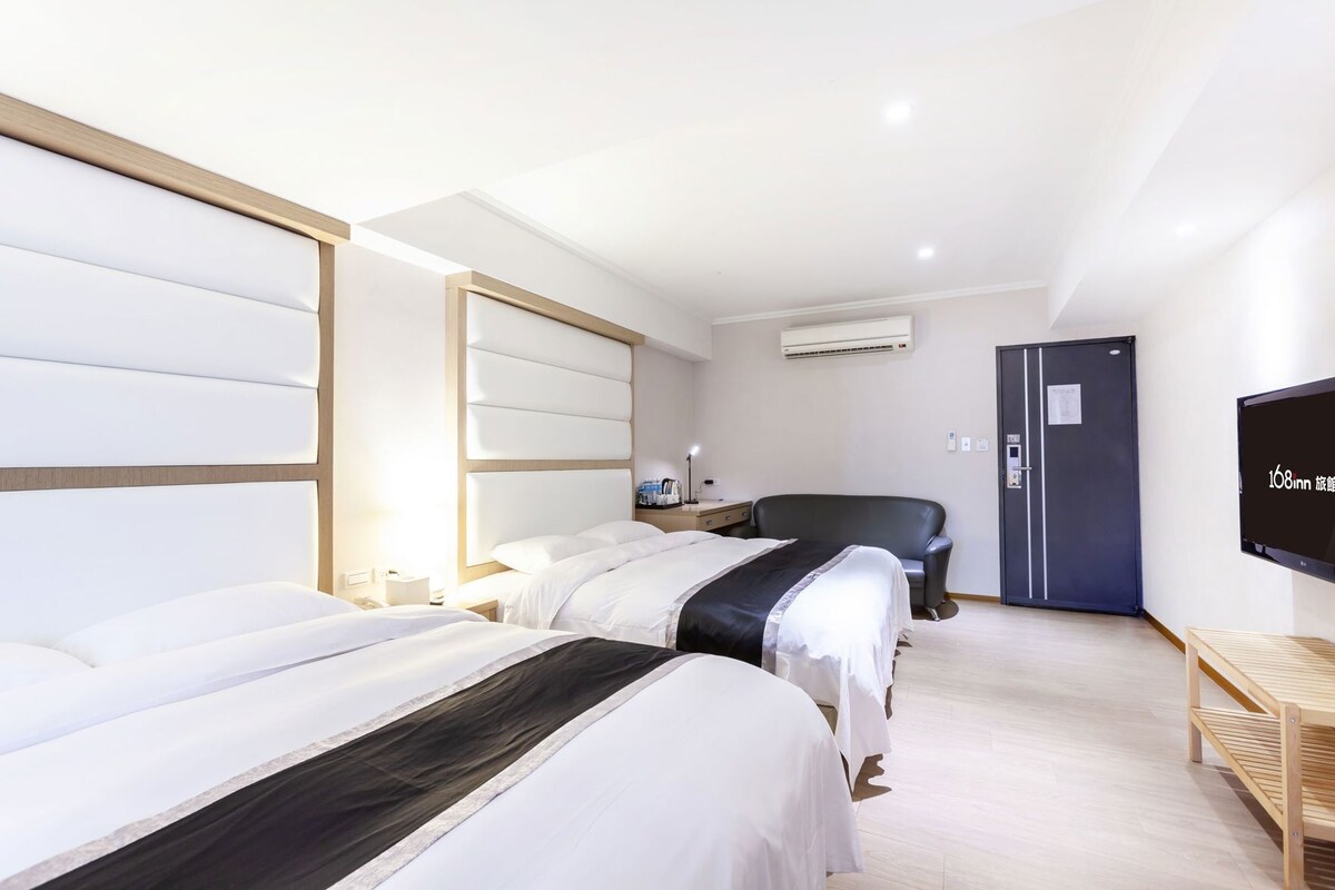 A hotel room with three beds, a desk, a chair, a TV, and a wardrobe.