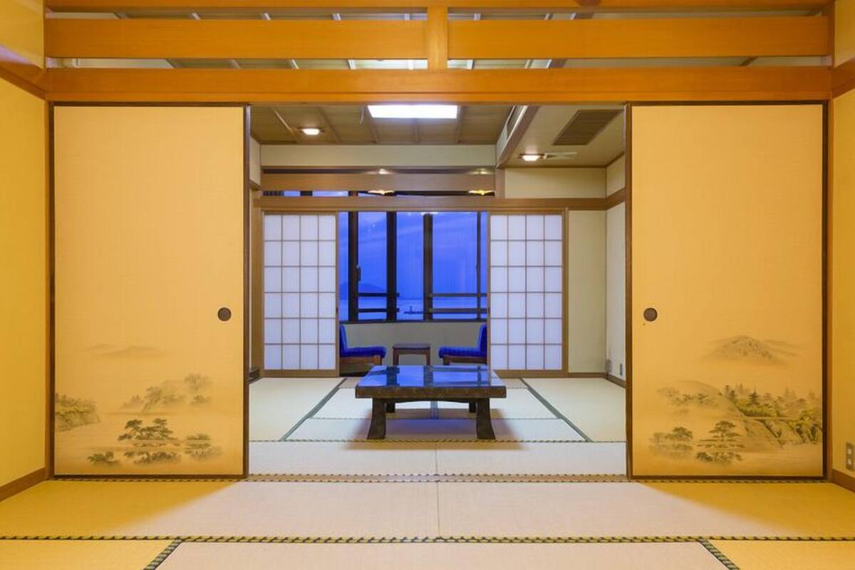 A traditional Japanese room with tatami flooring, sliding doors, and a view of a blue-lit room through a shoji screen.