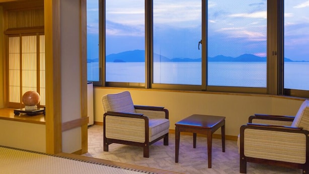 Une pièce avec vue sur un plan d’eau et des montagnes, comprenant deux fauteuils et une petite table.